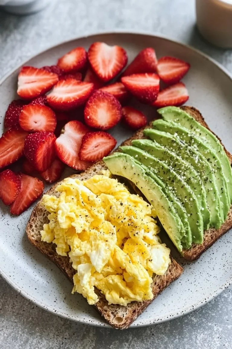 Delicious scrambled eggs served with strawberries and avocado toast on a plate.